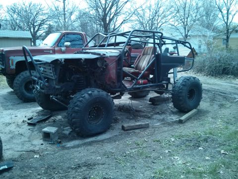 1986 Ford Bronco - A custom-built off-road buggy with a prominent roll cage sits beside a pickup truck, appearing to be under construction or modification.