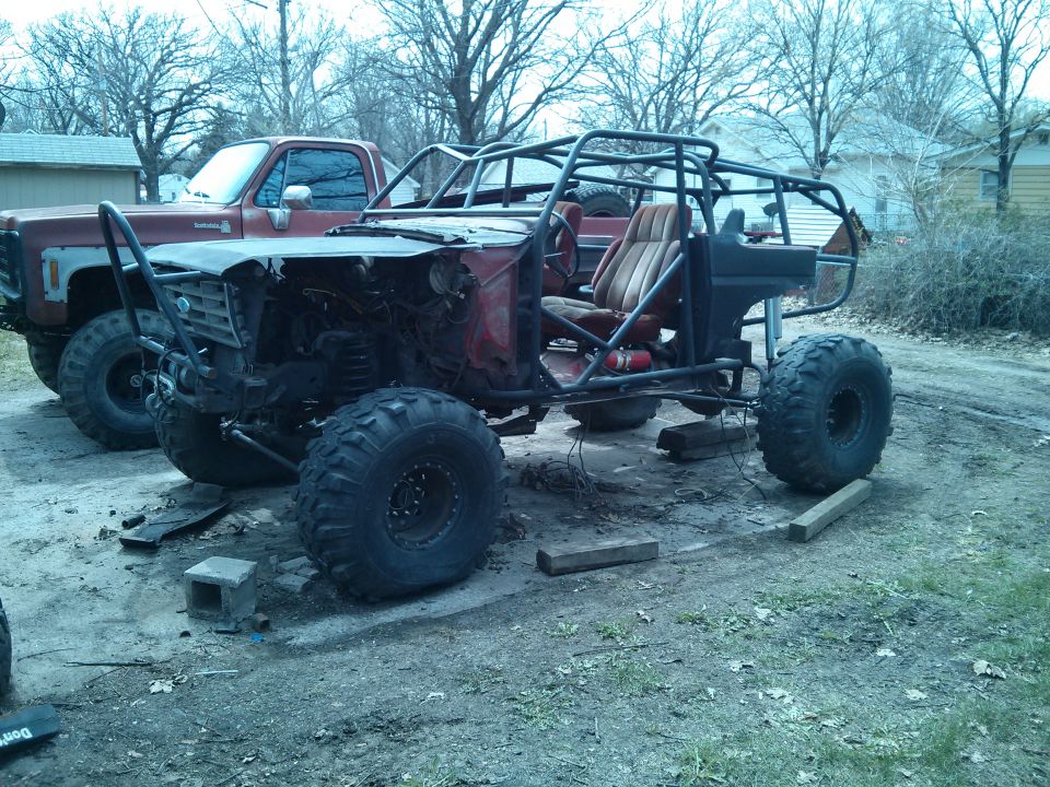 Custom off-road buggy with roll cage and large tires, parked next to a pickup truck