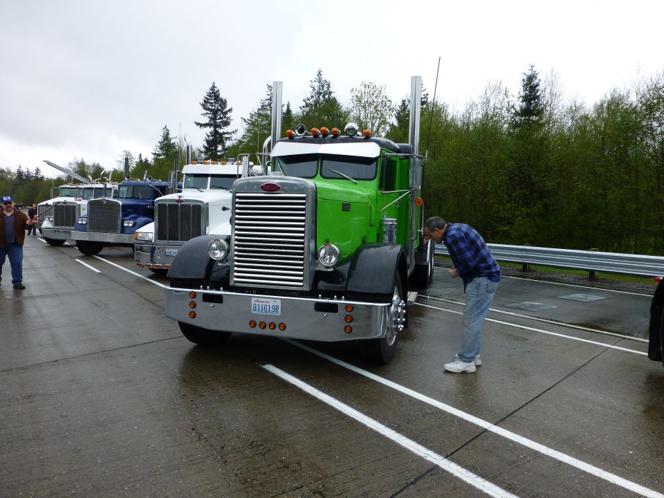 Green semi-truck with chrome grille, man looking at it. Other trucks in background