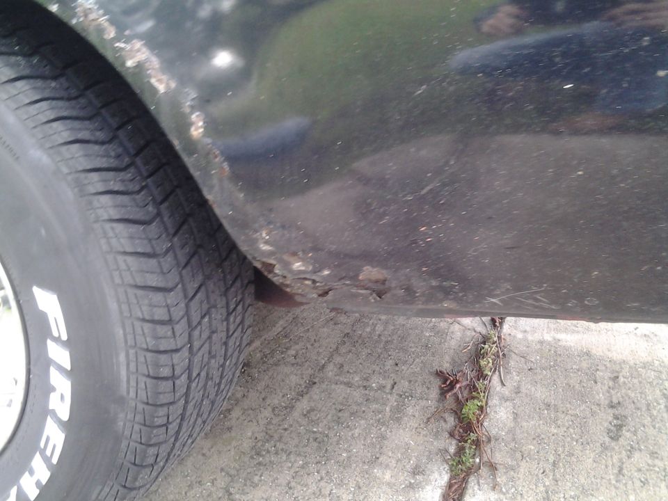 Close-up of a car's rear fender showing rust and a Firestone tire