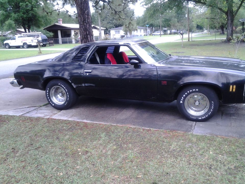 Black 1975 Chevrolet Chevelle coupe parked on a driveway, side view, with red and blue interior visible