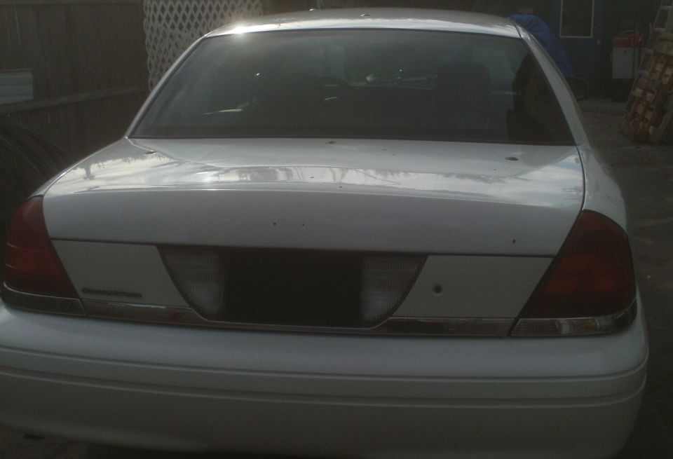 Rear of a white Ford Crown Victoria. Chrome trim across the trunk
