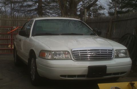 2006 Ford Crown Victoria - This white Ford Crown Victoria is parked in front of a wooden fence on a cloudy day.