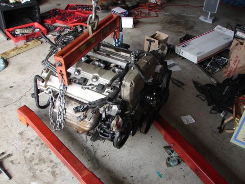 1992 Ford Taurus - An engine is suspended by a hoist, resting on a stand in a cluttered garage environment.