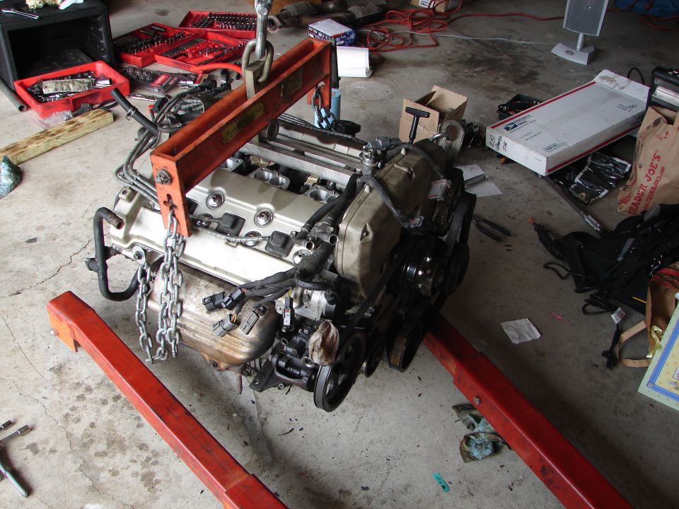 Engine being lifted by an engine hoist in a garage with tools and boxes around