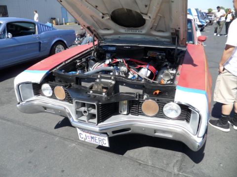1973 Ford Ranchero - Front view of a 1970s Ford car with its hood open, revealing the engine bay. A blue car is visible to the left.