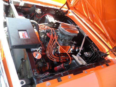 1973 Ford Ranchero - Engine bay of an orange vehicle, a chrome air cleaner and orange spark plug wires, with a photo album on the side.