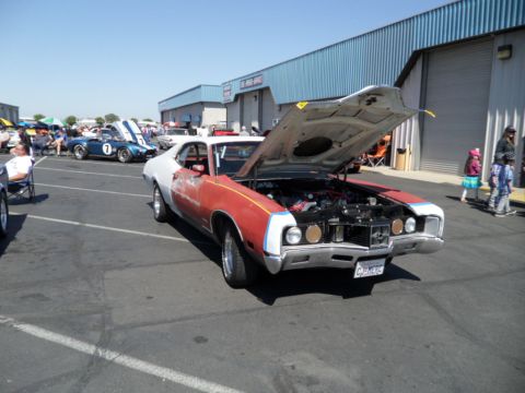 1973 Ford Ranchero - A two-tone red and white vehicle with its hood open is parked at an outdoor event, with other cars and people in the background.