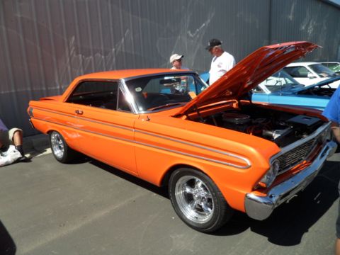 1973 Ford Ranchero - Orange 1964 Ford Falcon coupe at a car show, hood open, with other vehicles nearby.