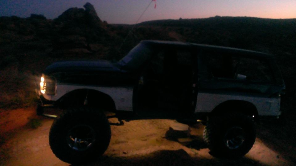 Dark green and white Ford Bronco with lifted suspension and large tires, parked on dirt at dusk