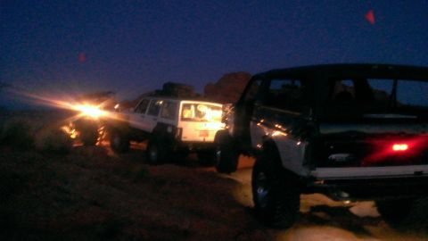 1994 Ford Bronco - A convoy of SUVs, including a 1994 Ford Bronco, travels off-road at dusk.