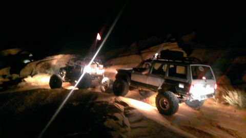 1994 Ford Bronco - Two SUVs navigate a challenging rocky path under the cover of darkness, illuminated by their headlights.