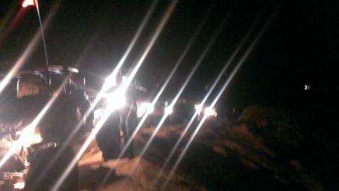 1994 Ford Bronco - Several off-road vehicles are driving on a dirt path at night, illuminated by their headlights.