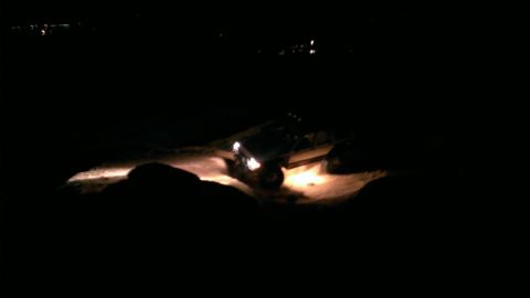 1994 Ford Bronco - A vehicle navigates a dirt path in the dark, illuminated by its headlights.