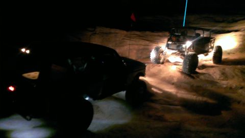 1994 Ford Bronco - Off-road vehicles navigate a dirt trail in the dark, with headlights cutting through the night.