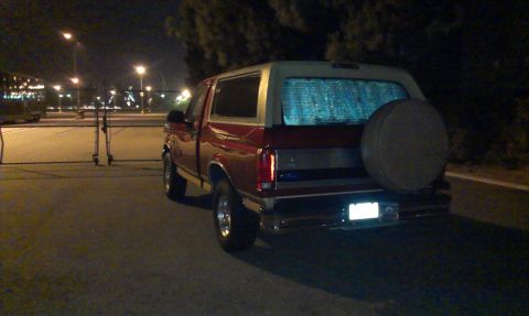 1994 Ford Bronco - This red Ford Bronco is parked at night, displaying its rear end with a spare tire mounted on the tailgate.