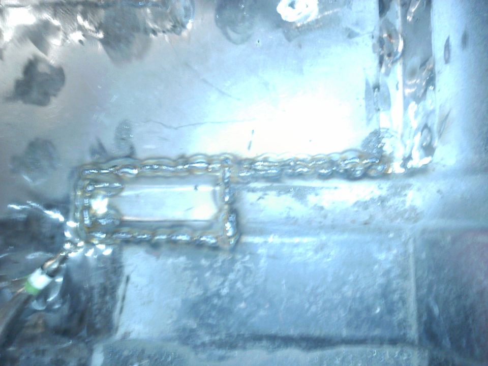 Close-up of a metal frame with visible welding. A small green wire is attached