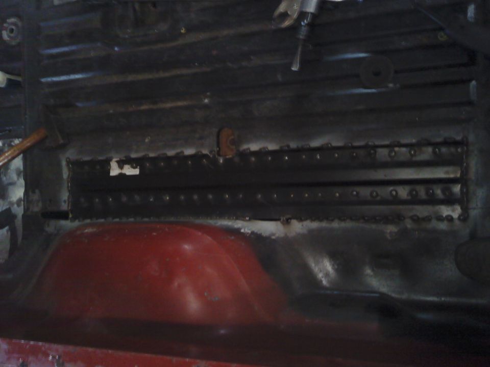 Interior floor pan with red wheel well, black ribbed metal, and visible rivets