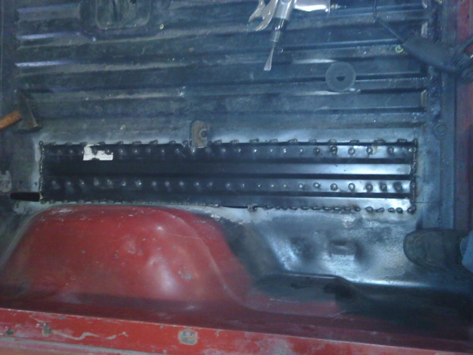 Interior view of vehicle floor with metal reinforcement and red wheel well