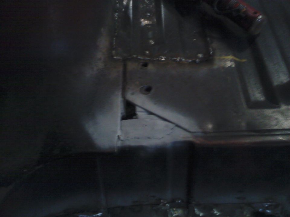 close-up of a dark, possibly rusty, vehicle undercarriage with some metal bracing and holes