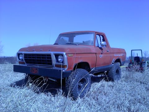 1978 Ford Bronco - This 1978 Ford Bronco is shown in a three-quarter front view, parked in a field with a tractor behind it.
