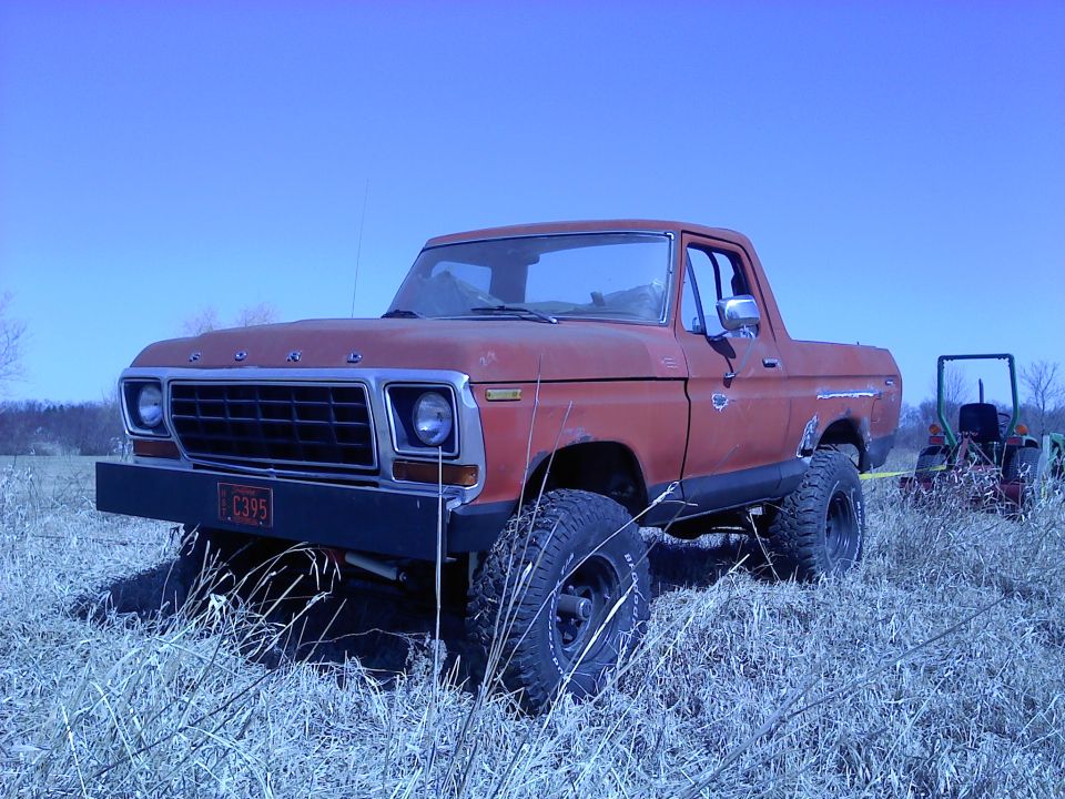 Red 1978 Ford Bronco parked in a grassy field with a tractor in the background