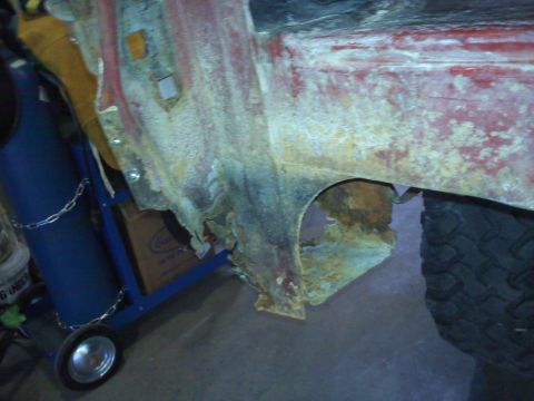 1978 Ford Bronco - The heavily corroded side panel of a vehicle shows significant rust damage around the wheel well.