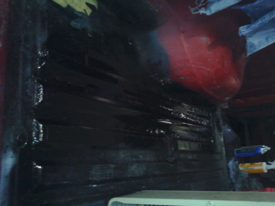 Looking into the dark interior of a vehicle, possibly a truck bed or cargo area, with some red paint visible on the upper right