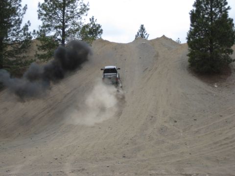 2005 Jeep Wrangler - A white pickup truck ascends a steep dirt hill, leaving a trail of dust and dark exhaust smoke.