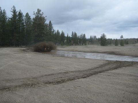 2005 Jeep Wrangler - A Jeep Wrangler navigates a muddy track, kicking up a large cloud of dust and spray.