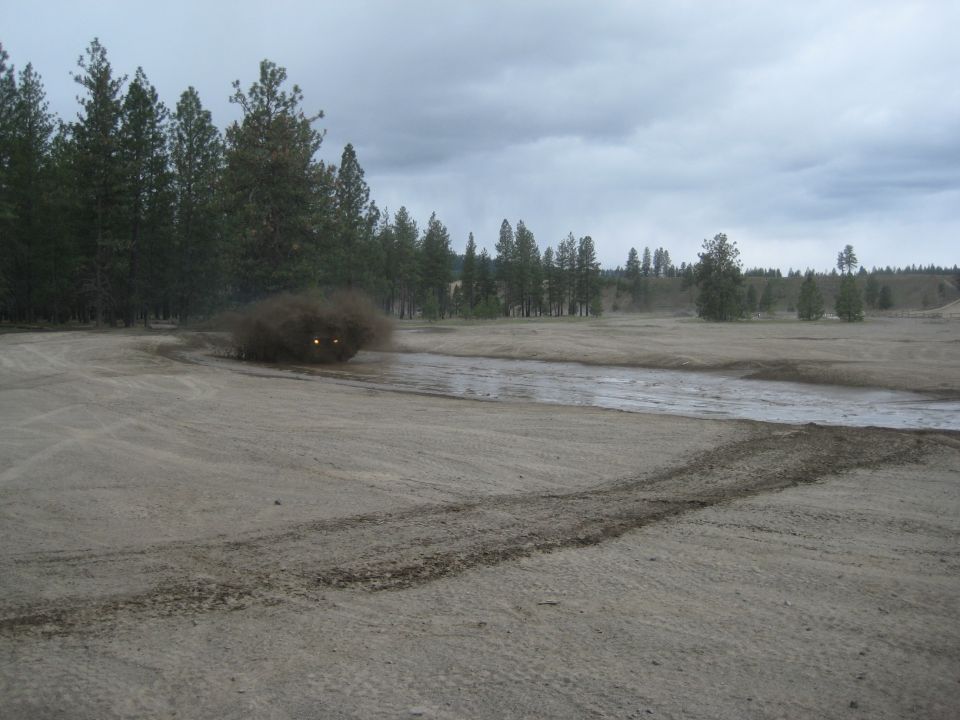 Jeep Wrangler kicking up dust and mud on a dirt track
