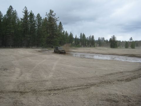 2005 Jeep Wrangler - Jeep Wrangler driving through a muddy track with trees in the background.