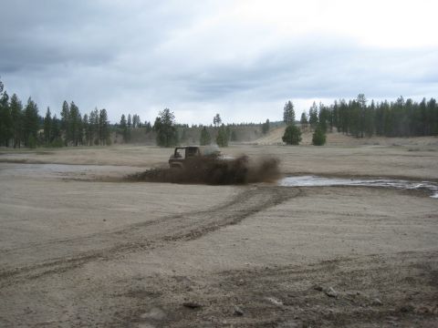 2005 Jeep Wrangler - A vehicle navigates a muddy terrain, creating a large spray of dirt and water.