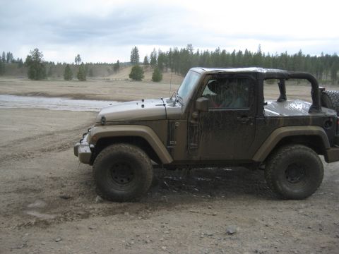 2005 Jeep Wrangler - A muddy Jeep Wrangler navigates an off-road trail under a cloudy sky.
