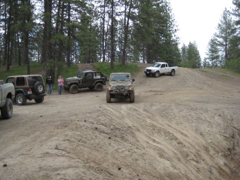 2005 Jeep Wrangler - A tan 2005 Jeep Wrangler is seen from the front on a dirt hill, with other vehicles in the background.