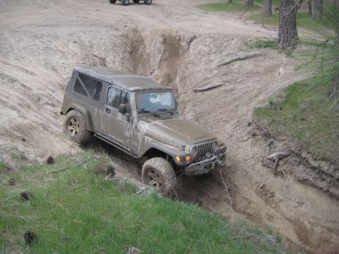 2005 Jeep Wrangler - A Jeep Wrangler is shown navigating a challenging off-road trail with steep inclines and muddy terrain.