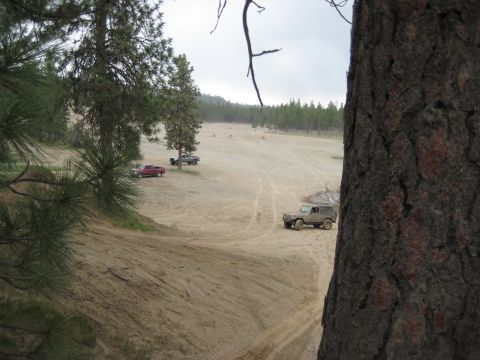 2005 Jeep Wrangler - Several vehicles are present in a sandy off-road area with trees in the distance.