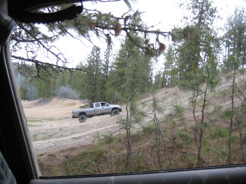 2005 Jeep Wrangler - A silver pickup truck navigates an off-road trail, kicking up dust and smoke.