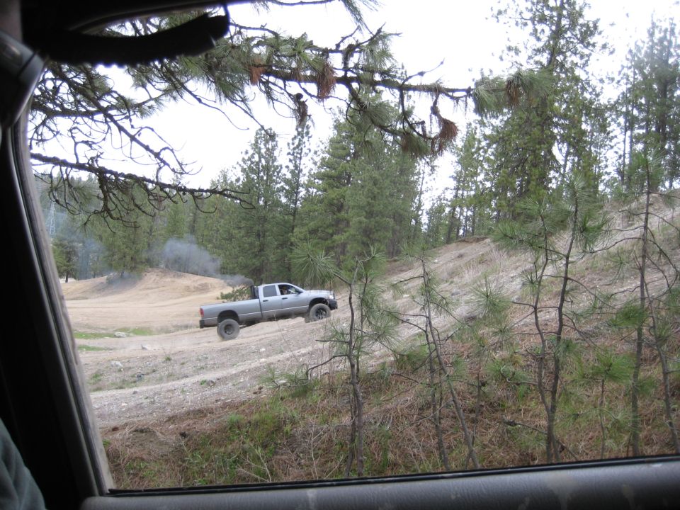 Silver pickup truck driving up a dirt hill, emitting black smoke from the exhaust