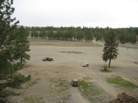 2005 Jeep Wrangler - Several vehicles are spread out across a dusty, open area surrounded by pine trees under an overcast sky.