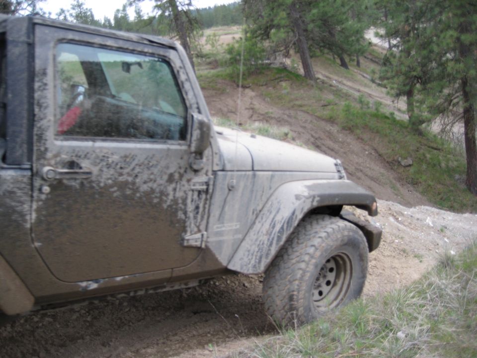 Mud-covered Jeep Wrangler, 3/4 front view, off-road tires, on a dirt path