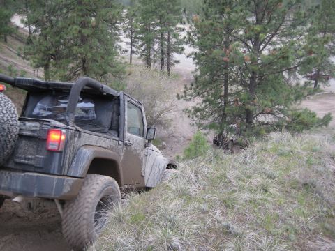2005 Jeep Wrangler - A muddy Jeep Wrangler navigates a challenging off-road trail, with another vehicle partially visible in the background.