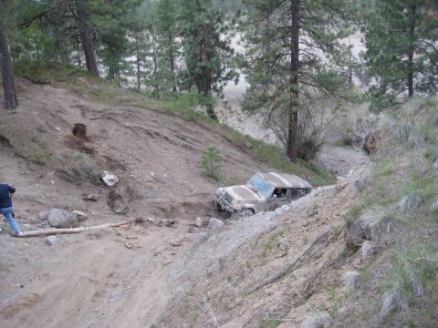 2005 Jeep Wrangler - An off-road vehicle is stuck on a steep, muddy incline surrounded by trees and dry brush.