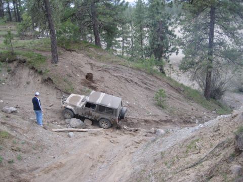2005 Jeep Wrangler - A tan 2005 Jeep Wrangler tackles a challenging off-road trail on a sunny day, with a bystander observing the ascent.