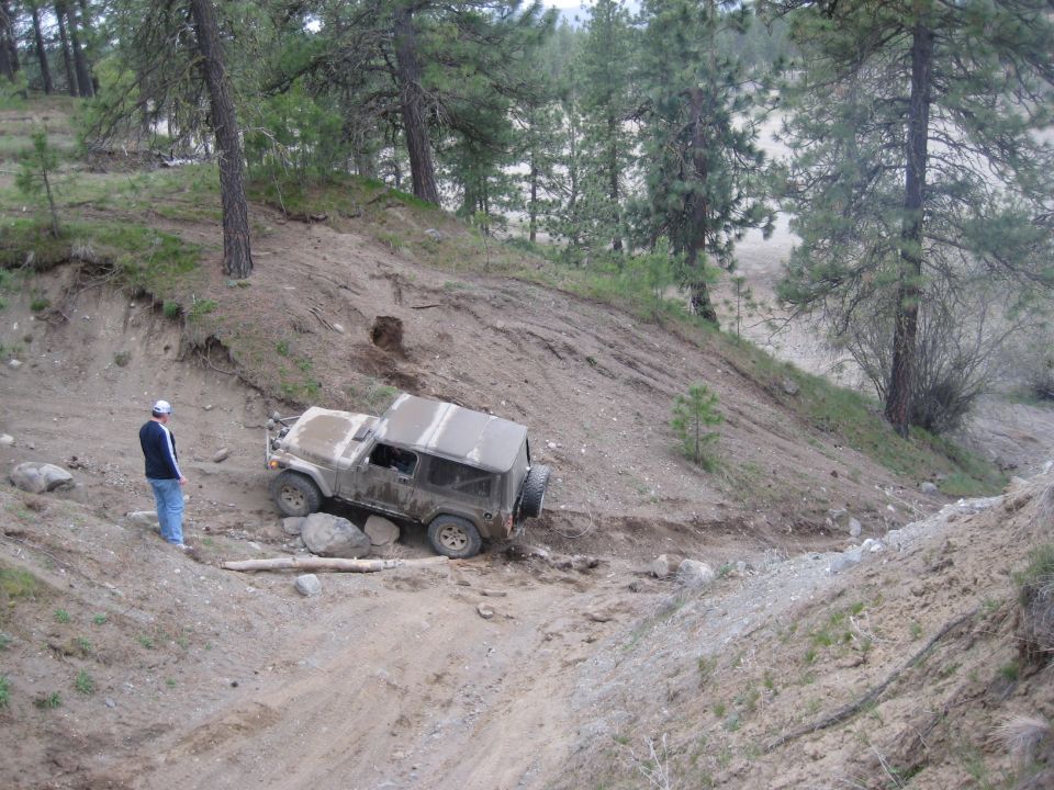 Tan 2005 Jeep Wrangler navigating a steep, rocky dirt trail with a person standing nearby
