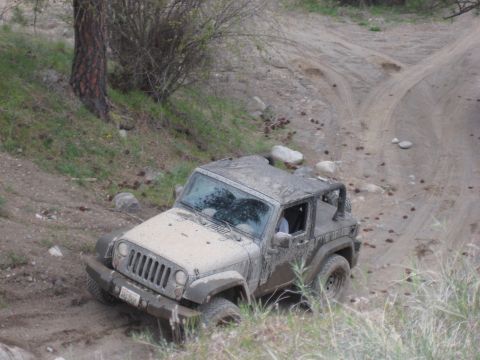 2005 Jeep Wrangler - A mud-splattered Jeep Wrangler navigates a challenging off-road trail.