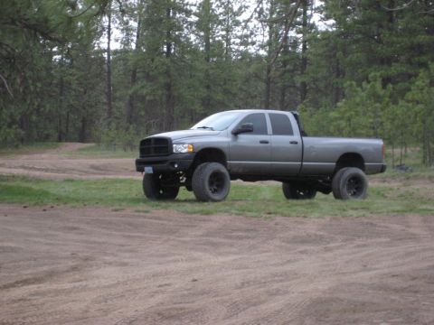 2005 Jeep Wrangler - A lifted, four-door pickup truck sits parked in a wooded area on a dirt path.