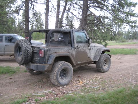 2005 Jeep Wrangler - A mud-covered Jeep Wrangler is parked off-road next to another vehicle.