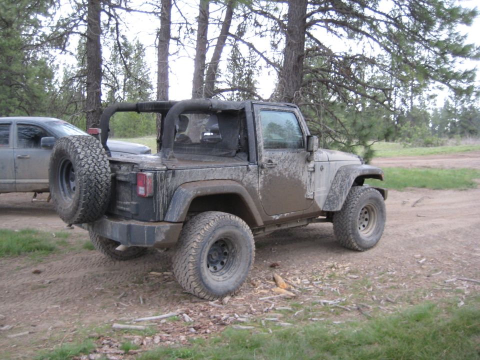 Mud-splattered Jeep Wrangler, 3/4 front view, soft top removed, spare tire on rear door