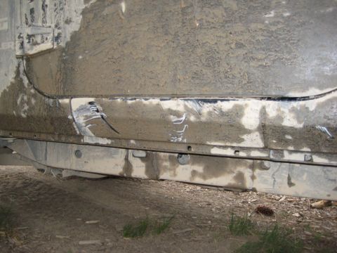 2005 Jeep Wrangler - Close-up of a heavily soiled vehicle side panel showing damage and undercarriage components.